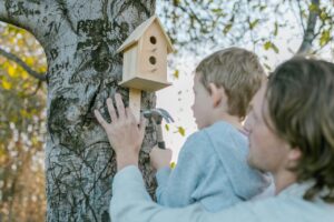 Een kind en ouder hangen een vogelhuisje op